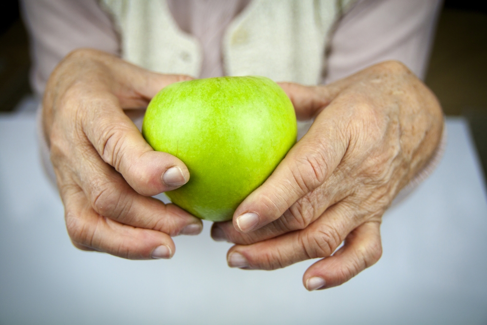 An older woman's hands, showing damage from rheumatoid arthritis, holding a green apple.