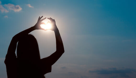Woman-making-heart-sign-over-sun